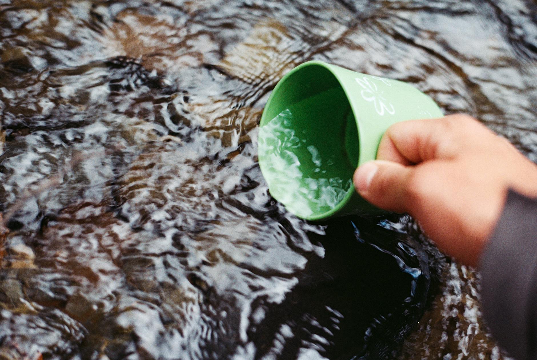 Person, Die Wasser Mit Grünem Becher Schöpft